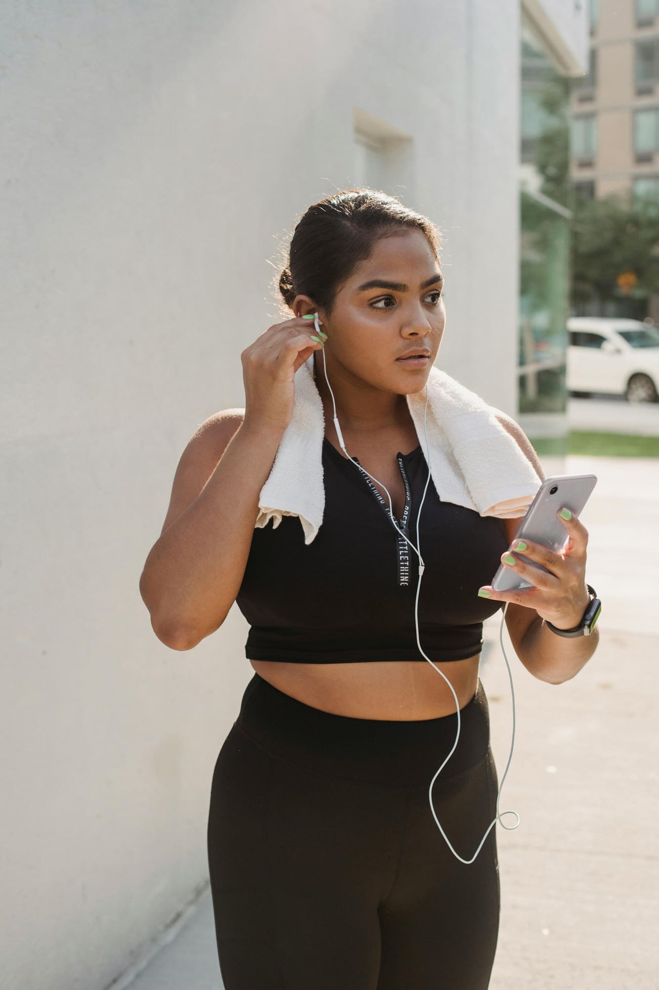 Woman wearing workout attire with a towel around her neck listening to music through headphones while holding her phone.